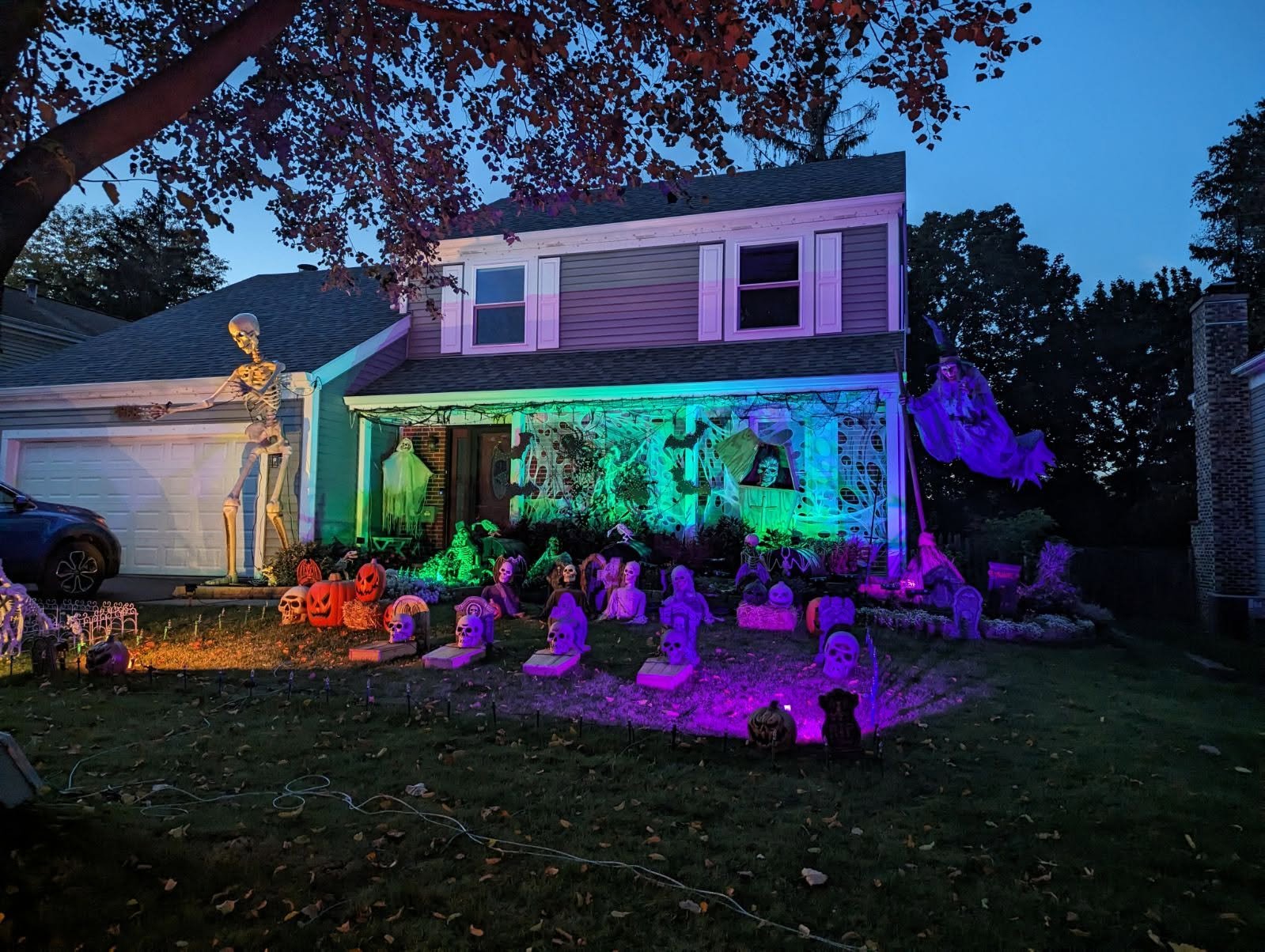 Germann Lights Halloween display lit in purple and green with a giant skeleton, pumpkins, a graveyard, and a flying witch